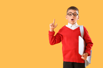 Shocked little schoolboy with laptop pointing at something on yellow background