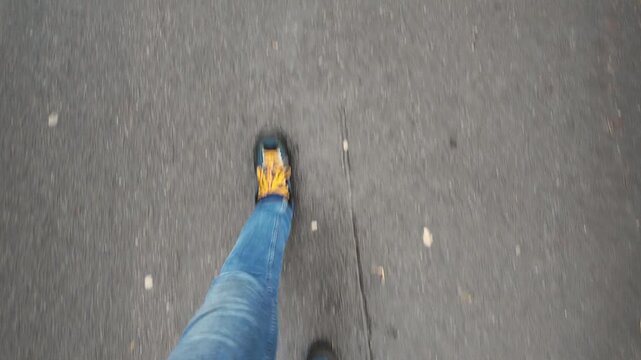 pov walking on asphalt with sneakers, jeans. overhead closeup showing single leg stepping across marked pavement, steady rhythm, casual commuter pace, neutral daylight, urban minimalism vibe, focus
