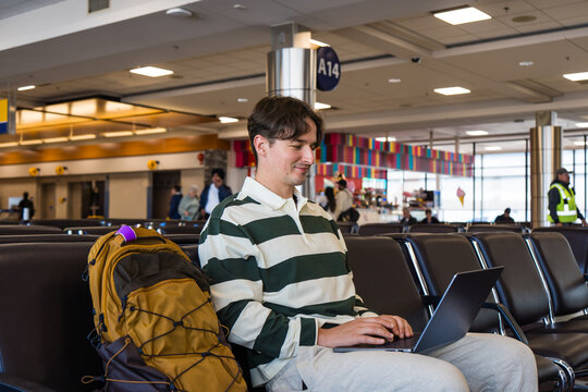 Young man working on his laptop while waiting at the airport terminal. - Powered by Adobe