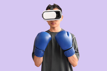 Sporty young Asian man in VR glasses with boxing gloves on lilac background