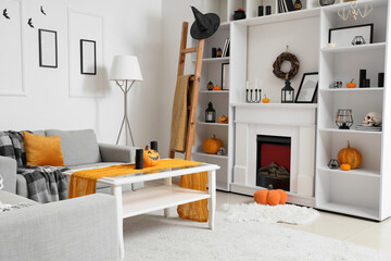 Fototapeta premium Interior of light living room decorated for Halloween with sofas, shelf unit and fireplace