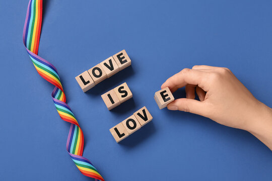Female hand with text LOVE IS LOVE and rainbow ribbon on blue background. LGBT concept