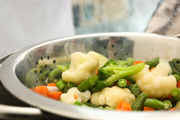 Frozen mixed vegetables steaming in metal colander, closeup