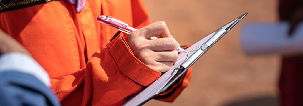 Action of an engineer is writing maintenance service detail on the paper checklist during performing the job. Industrial working scene, close-up with selective focus on hand.