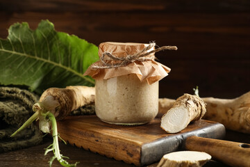 Jar with horseradish sauce, roots and leaf on wooden background