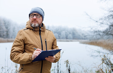 Ecologist monitors the environment of a winter forest and a snow-covered river. Observing animals...