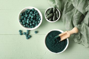 Bowls of spirulina powder with capsules and tablets on green wooden background
