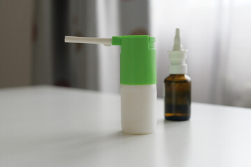 A colorful container for liquid spray stands on a table next to a small glass bottle filled with solution. Sunlight fills the room softly