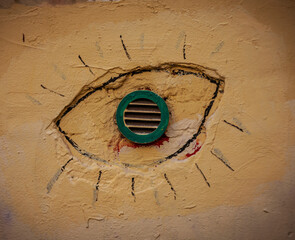 Ventilation grille on the wall of an old house stylized as an eye.