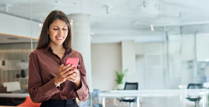 Young business woman manager user using cell phone mobile app. Smiling Latin Hispanic mature female businesswoman holding smartphone in office trading, working online at workspace. Banner, copy space