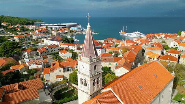 Aerial view of Postira, Brac Island, Croatia. Terracotta roofs meet the deep blue Adriatic under dramatic skies. A picturesque harbor town, blending history with modern tourism.