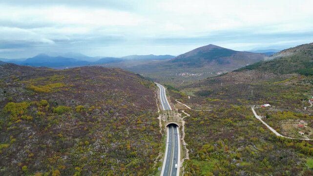 An aerial view of the A1 motorway winding through the Dinaric Alps in Croatia, adorned with autumn colors under an overcast sky. A modern road trip through rugged beauty.