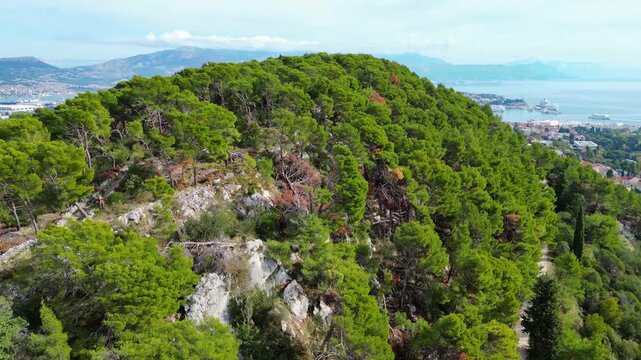 Split, Croatia: A stunning aerial panorama of the historic city, bustling harbor, and lush Marjan Hill. Adriatic beauty under a dynamic sky.