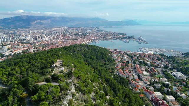 Split, Croatia: A stunning aerial panorama of the historic city, bustling harbor, and lush Marjan Hill. Adriatic beauty under a dynamic sky.