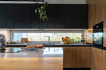 Interior of modern kitchen at smart home with luxurious furniture, wooden cabinet and black counter with sink near window.