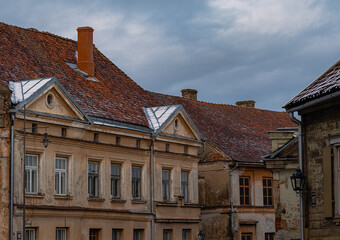 Old weathered European town houses with red tiled roofs and cloudy sky, vintage historic architecture cityscape background