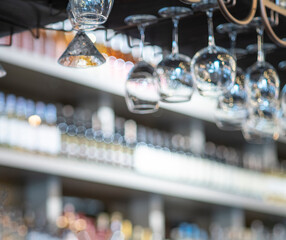 Elegant upside-down wine glasses hang from a sleek overhead rack in a modern bar or upscale restaurant. 