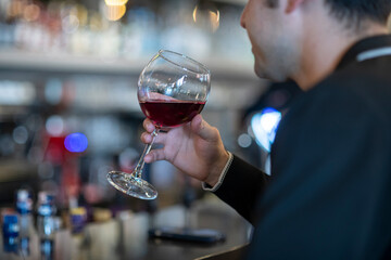 A sophisticated man in a dark sweater holds a glass of rich red wine, gazing thoughtfully in a stylish, dimly lit bar. 