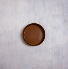 Top view of a single empty, rustic brown ceramic plate centered on a textured light gray concrete background. 