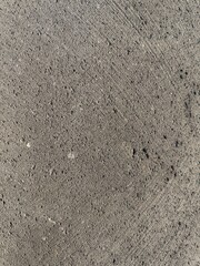 Close-up of a dark gray concrete or asphalt surface with a rough texture and imperfections. Tool or cleaning marks are visible on the surface. Ideal for background, abstract, industrial.