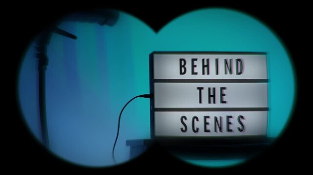 A cinematic view of a Behind the Scenes sign on a wooden stool under professional studio lighting. The frame includes a timestamp and recording elements mimicking a video camera interface. Close up.