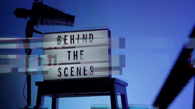 A cinematic view of a Behind the Scenes sign on a wooden stool under professional studio lighting. The frame includes a timestamp and recording elements mimicking a video camera interface. Close up.