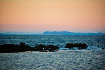 Sunset Coastal View with Distant Snowy Mountains and Rocky Shore