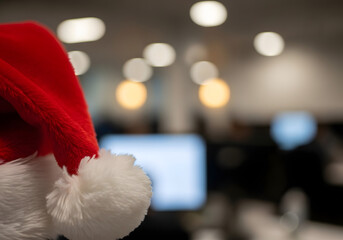 Gorro de Papá Noel rojo en primer plano sobre fondo de oficina moderna desenfocada con luces bokeh y amplio espacio para texto de felicitación corporativa navideña