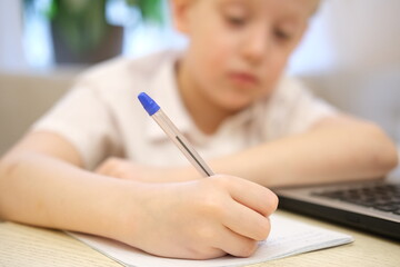 Young boy writing homework and studying with laptop