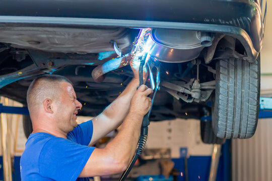 Mechanic welding car exhaust system in auto workshop - Powered by Adobe
