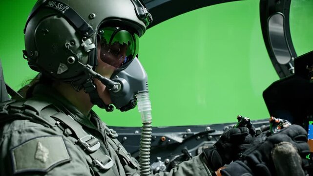 Professional fighter jet pilot wearing helmet and oxygen mask sitting in cockpit against green screen background for chroma key film production and military aviation simulation scenes
