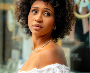 Close-up of a young African-American woman with curly hair, diamond necklace and white top, looking to the side with an expression of concern or uncertainty and sweetness
