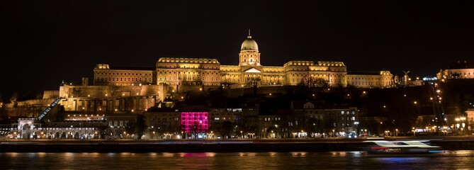 Buda Castle shines brightly at night along the Danube River in Budapest, Hungary