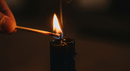 Atmospheric scene: match lights a black candle flame in dark room. Perfect for solemn reflections, Halloween, gothic themes, memorial services, or dramatic rituals.