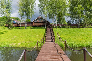 A wooden walkway connects a charming cabin to the water's edge, framed by tall trees and greenery. Dark clouds hint at a cool breeze, creating a calm atmosphere