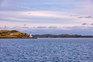 A picturesque lighthouse stands on an island in Halifax Harbour, framed by a serene sky and tranquil waters.