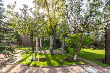 A peaceful park scene showcases lush green trees and sunlight filtering through leaves. The bright space invites relaxation and enjoyment of nature, making it perfect for a leisurely stroll