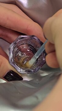 Brow and lash tint being mixed in small glass cup top view. beauty professional mixing tint in container to prepare cosmetic mixture for application for beauty tutorial, professional makeup procedures