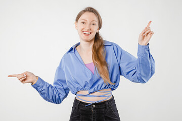 Pretty young female model in everyday clothing on plain white background pointing her index fingers aside for marketing message, ad placement or branding
