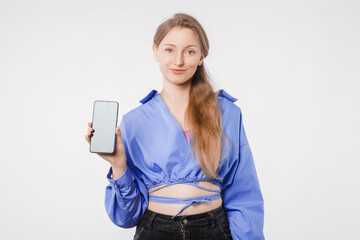 Joyful young woman showing smartphone screen, standing in studio on white background. Modern tech, app, design, advertising concept