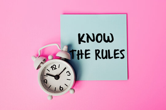 Know the Rules: text on a sticky note. Ideal for Educational Materials, Compliance Guidelines, Business Regulations and Legal Advisories. White alarm clock and Blue Note on a Pink Background