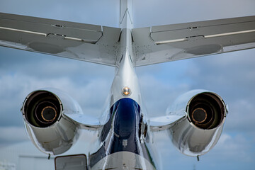 Rear view of a business jet on the apron, displaying both jet engines, landing gear, and open cargo hatch, selective focus used, focus on tail light.