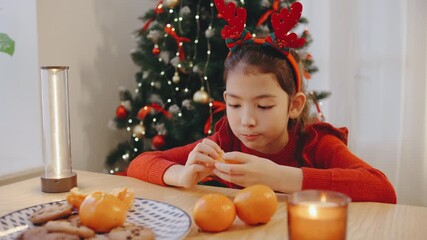 Girl enjoying festive cookies and oranges while celebrating Christmas and New Year near a decorated tree during the holiday season