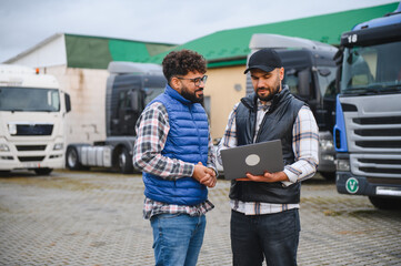 Truck drivers discussing logistics using laptop at fleet parking