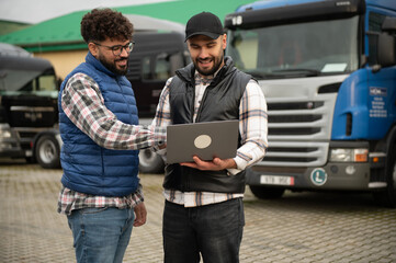 Truck drivers discussing logistics using a laptop outdoors