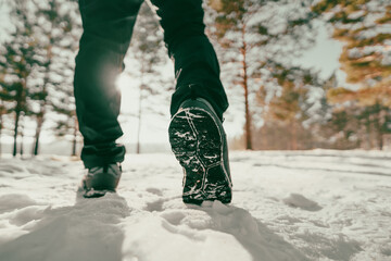 Fototapeta premium A winter walk through a snowy forest. A close-up of a person's feet in winter boots walking through the snow on a sunny, frosty day. The image conveys a sense of fresh air, outdoor activity