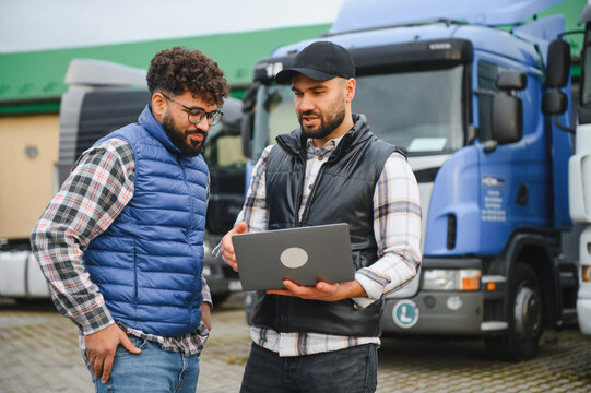 Truck drivers discussing logistics using laptop at fleet depot
