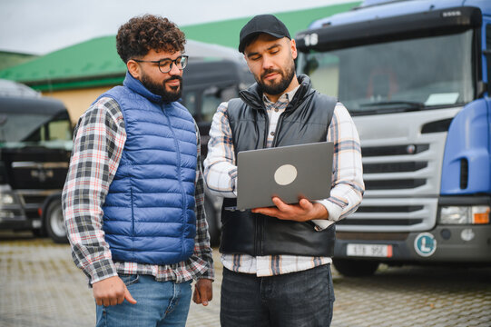 Truck drivers discussing logistics using laptop at fleet parking