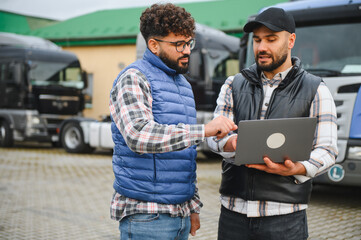 Truck drivers discussing logistics on laptop near vehicles