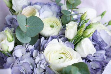 Close-up of elegant bouquet with white ranunculus, lisianthus, purple hydrangeas, and eucalyptus leaves in soft natural light

